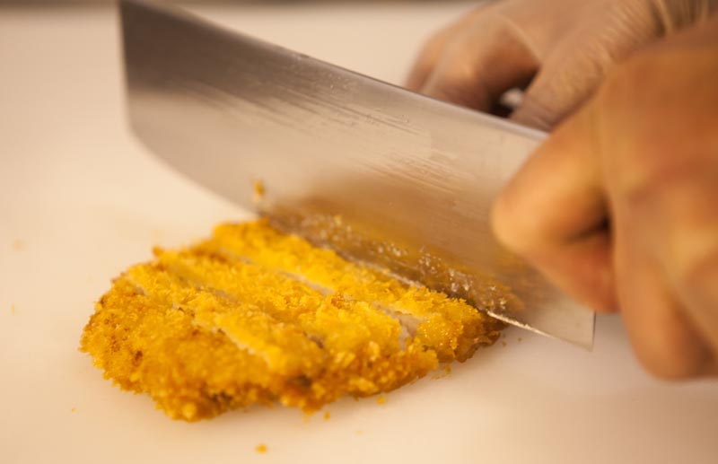 Katsu cutlet being prepared with love. Employee slices the cutlet expertly.