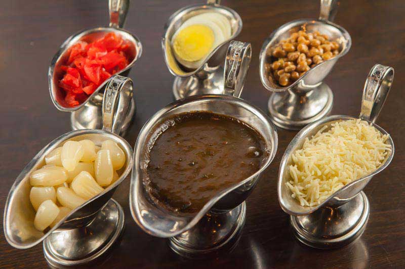 Top notch ingredients. Side dishes for the Japanese curry displayed in metal pourers, including rakkyo (pickled shallots), fukujinzuke (pickled radish), natto, boiled egg, and shredded cheese.including